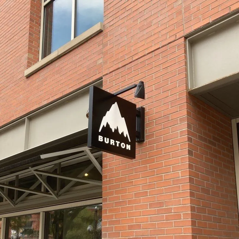 A Burton blade sign on a black bracket over the sidewalk