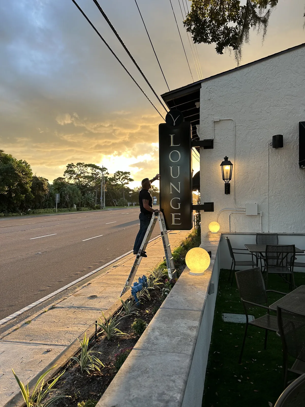 An installer mounting a vertical blade sign on a restaurant facade at sunset