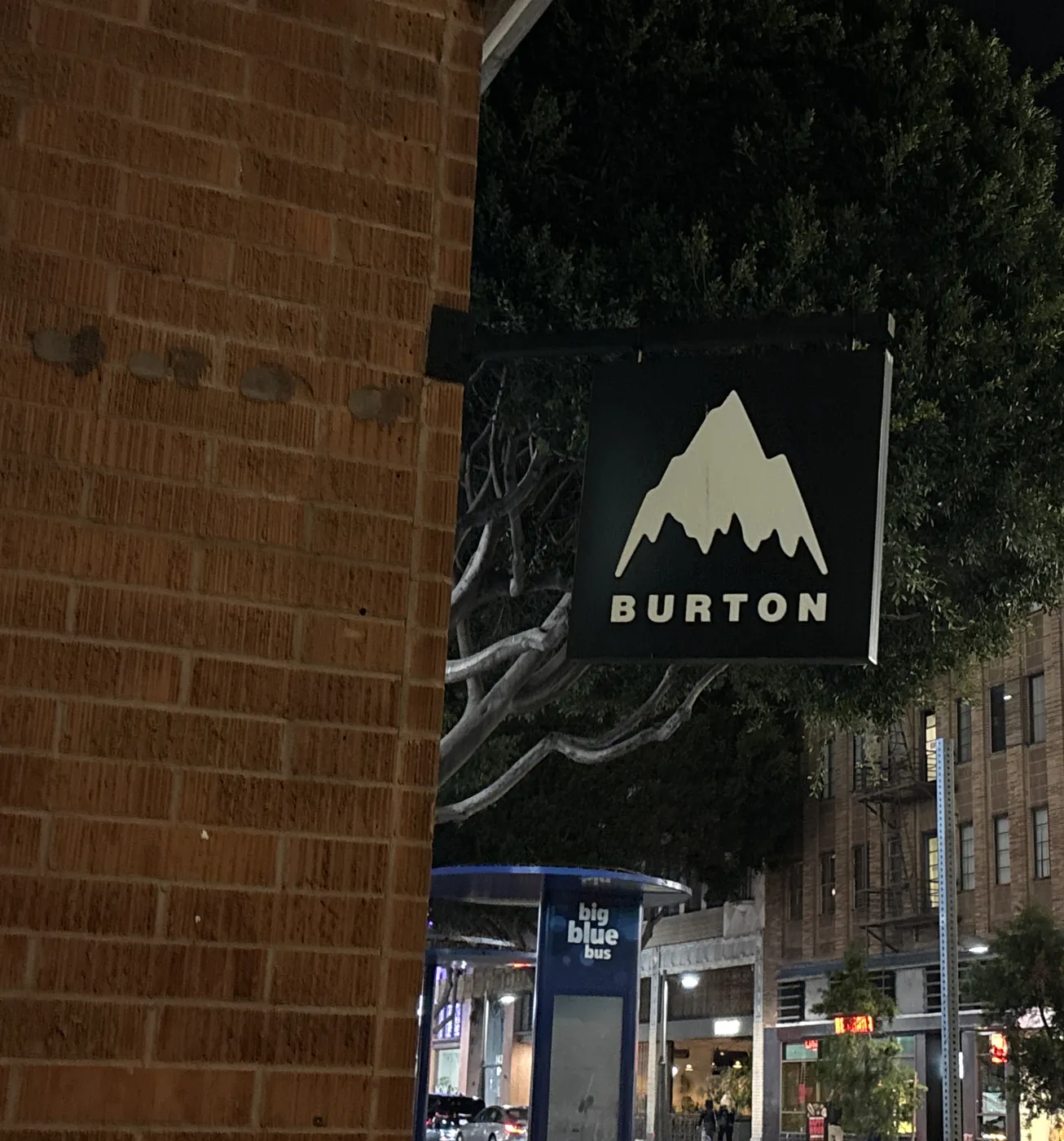 A Burton blade sign lit against a brick pier at night