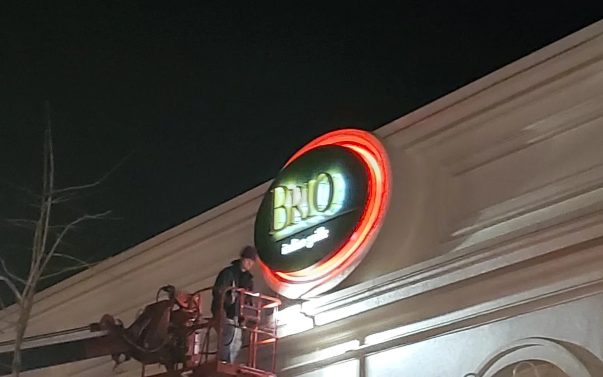 A National Sign Team installer in a bucket lift finishing the illuminated Brio sign at night