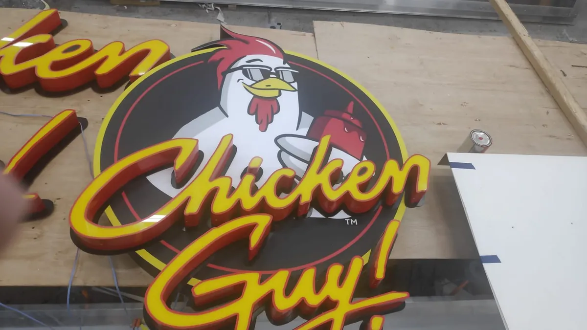 An illuminated Chicken Guy logo sign at dusk