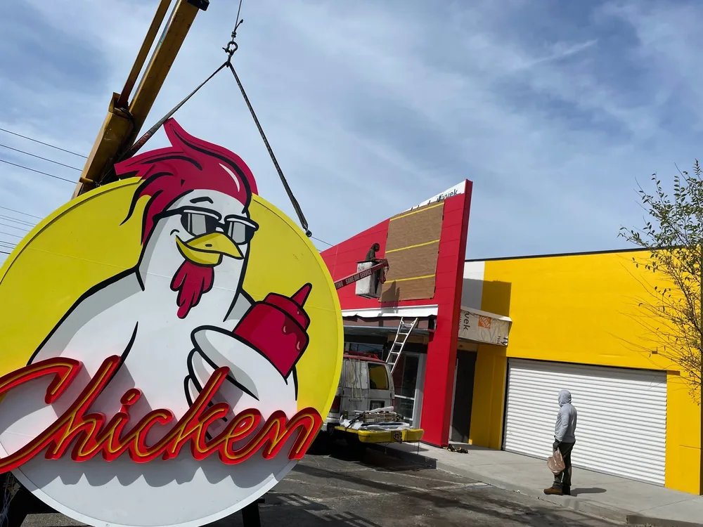 A Chicken Guy sign being lifted into place by a crane