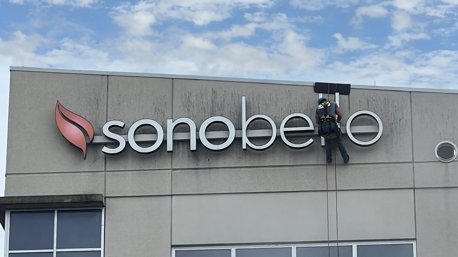 A man is cleaning the sign on the side of a building